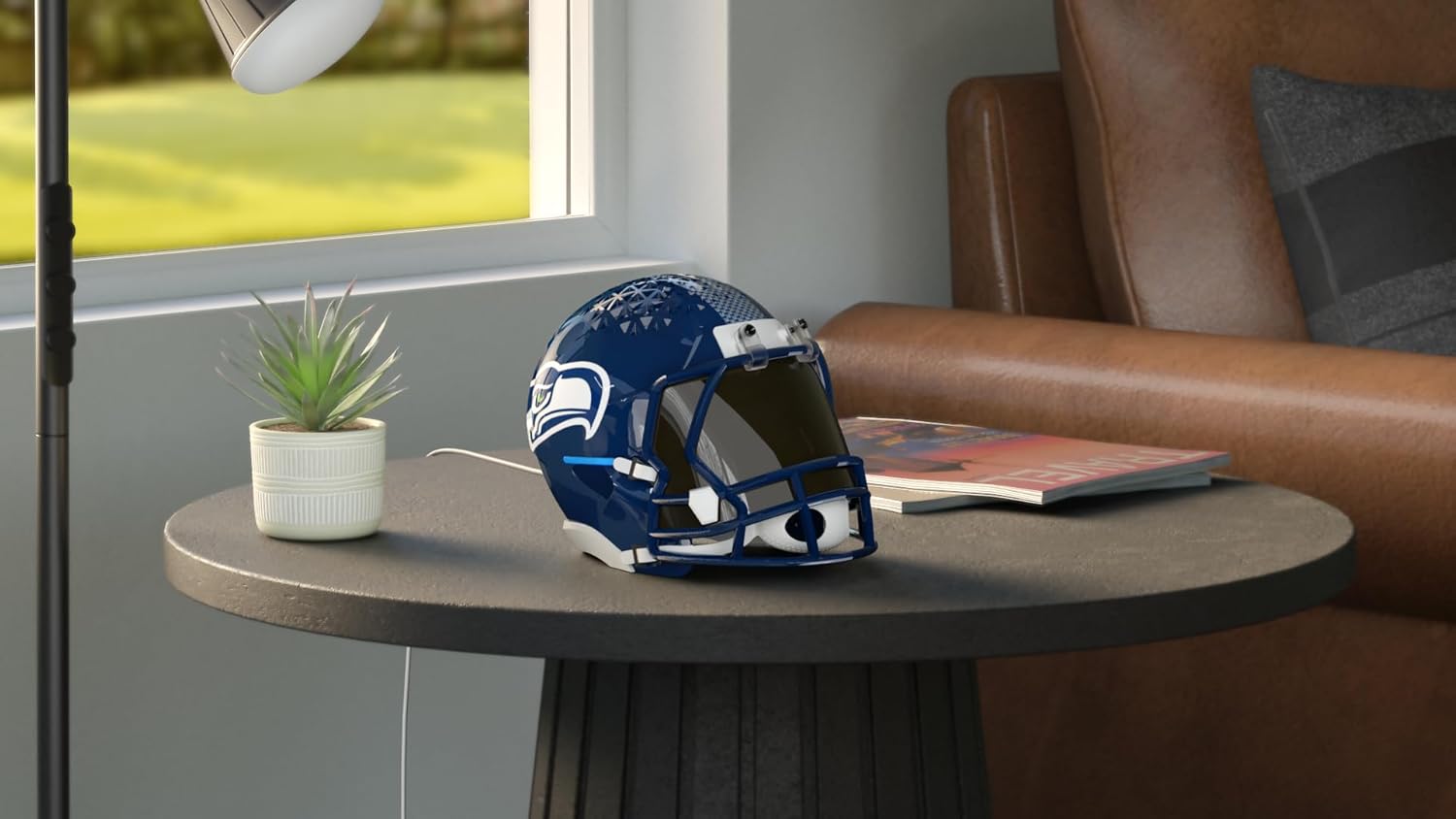 A blue and white NFL football helmet with a team logo sitting on a round gray table next to a small potted succulent plant, positioned by a window with brown leather chairs in the background.