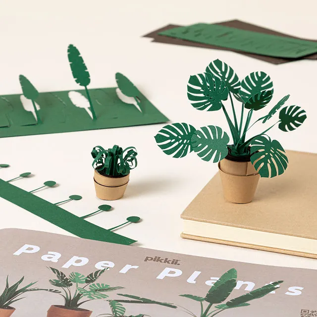 Unkillable Desk Plants paper DIY kits featuring miniature potted plants with green paper leaves in wooden pots, displayed alongside flat green paper plant cutouts and packaging labeled "paper plants."